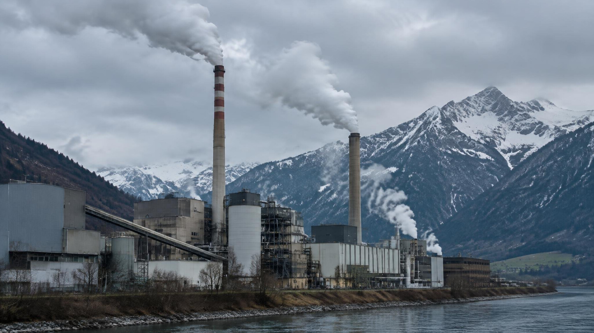 Industrial factory with smoke emitting from chimneys against a mountain backdrop